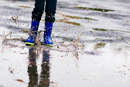 Happy little boy in rubber blue rainboots jumping to dirty puddle. Rainy autumn dayの写真素材