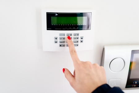 Young woman entering security code on home security alarm system keypad