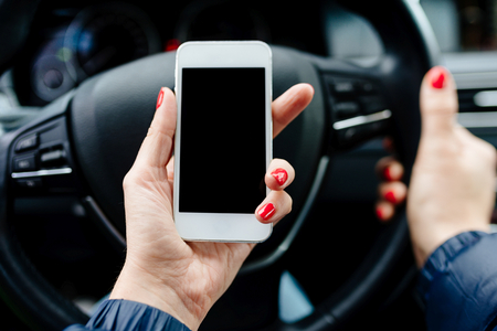 Woman in car holding a white smartphone with blank screen in her handの写真素材