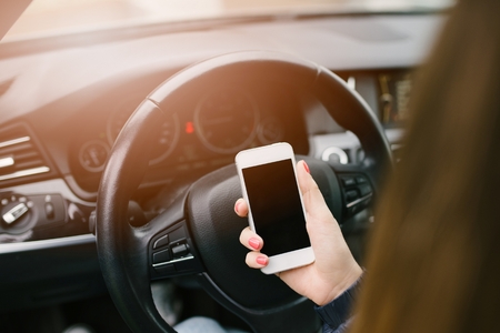 Woman in car holding a white smartphone with blank screen in her handの写真素材