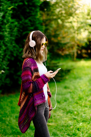 Portrait of a young woman in woolen sweater listening to music in parkの写真素材