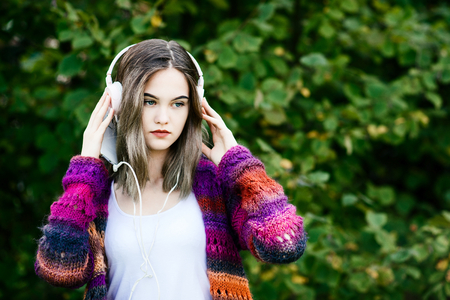 Portrait of a young woman in woolen sweater listening to music in parkの写真素材