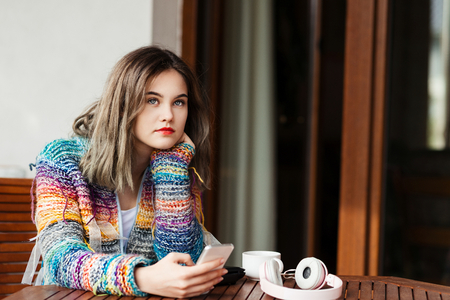 Young woman in woolen sweater uses a smartphone on home terrace.の写真素材
