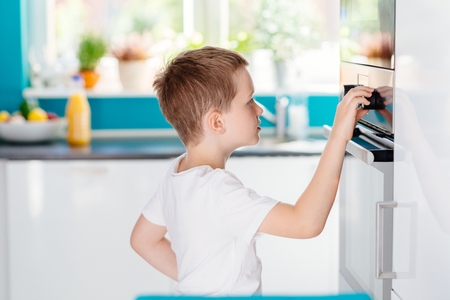 Child regulating temperature of the oven . Boy helping in the kitchen. Baking with childrenの写真素材