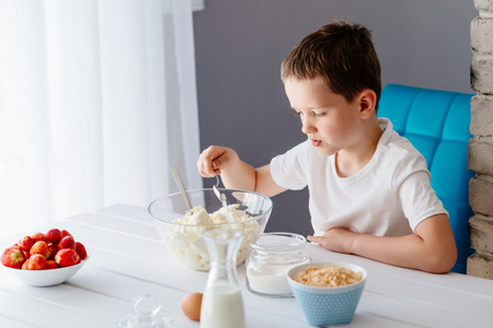 Boy adding sugar to white cheese in bowl for cheesecake. Child helping in the kitchen. Baking with childrenの写真素材