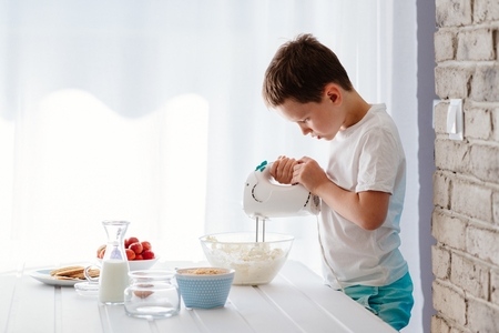 Child preparing cookies in kitchen. Mixing white cheese for cheesecake with hand mixer. Boy helping in the kitchen. Baking with childrenの写真素材