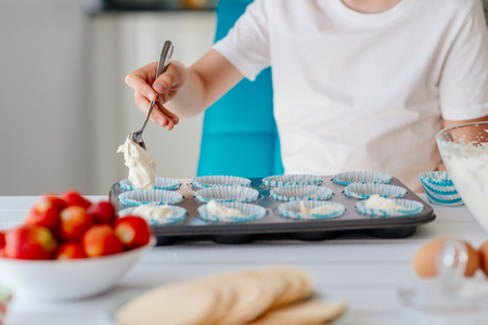 Child filling cupcakes form with dough ingredients. Boy helping in the kitchen. Baking with childrenの写真素材