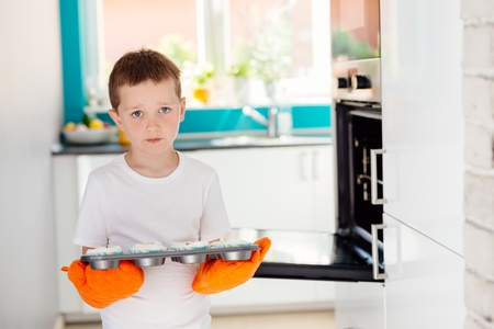 Child holding baking tray with cupcakes. Boy helping in the kitchen. Baking with childrenの写真素材