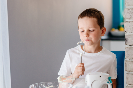 Child tasting pastry from mixer agitator . Boy helping in the kitchen. Baking with childrenの写真素材
