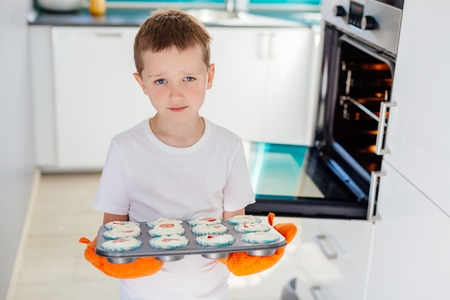 Child holding baking tray with cupcakes. Boy helping in the kitchen. Baking with childrenの写真素材