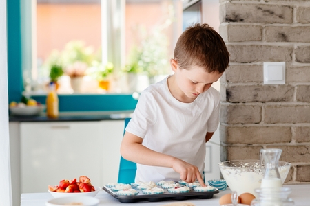 Child filling cupcakes form with dough ingredients. Boy helping in the kitchen. Baking with childrenの写真素材