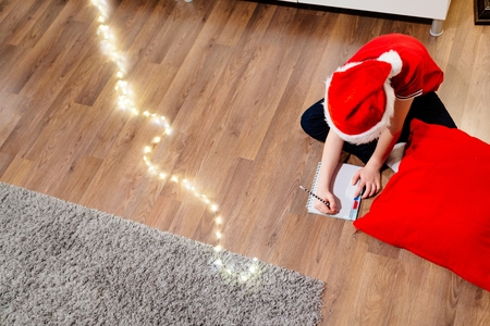 Boy writing a letter to Santa Claus. Wears red Santa Claus hat and red polo shirtの写真素材