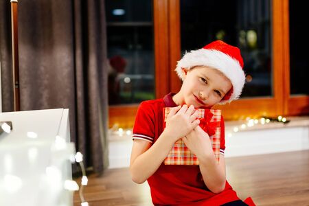 Little boy in red Santa Claus cap holding a Christmas giftの写真素材