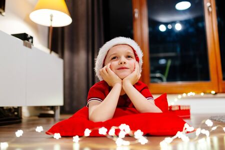 Little boy in red Santa Claus cap dreaming about Christmas giftsの写真素材