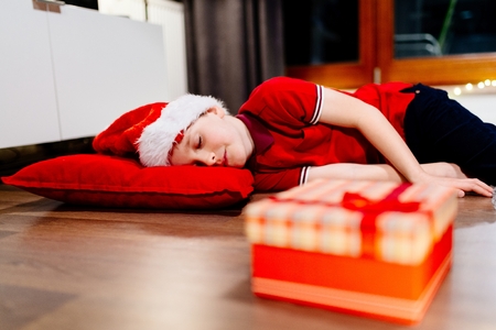 Little boy in red Santa Claus cap dreaming about Christmas giftsの写真素材
