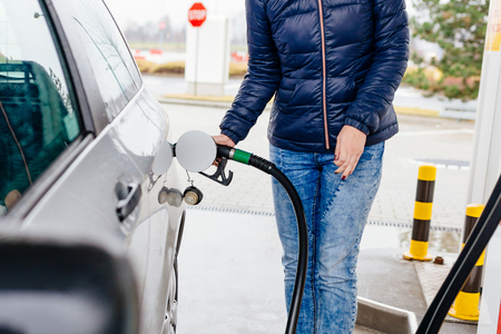 Woman refueling her small silver car at the gasoline stationの写真素材