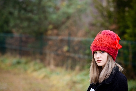 Thoughtful young woman in woolen red cap in gardenの写真素材
