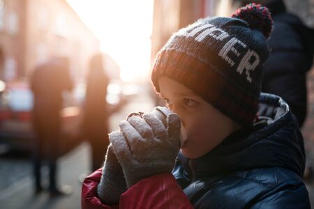 Little 7 years old boy drinking hot cocoa from paper mug outdoorsの写真素材
