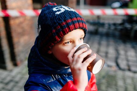 Little 7 years old boy drinking hot cocoa from paper mug outdoorsの写真素材