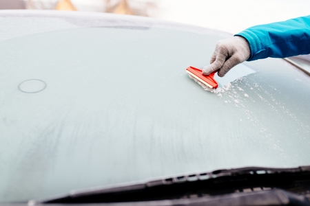 Woman deicing front car windshield with scraper. Car at winterの写真素材