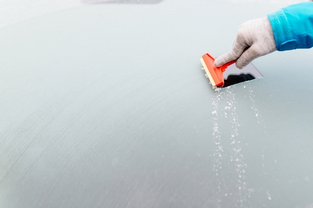 Woman deicing front car windshield with scraper. Car at winterの写真素材