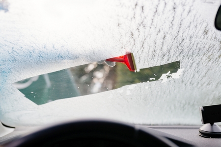 Woman deicing front car windshield with scraper. Car at winter. View from insideの写真素材