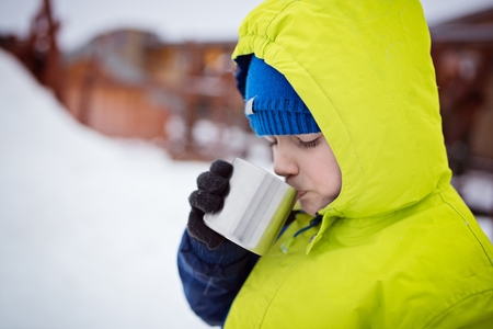 Child drinking hot tea from the metal mug. Wintertimeの写真素材