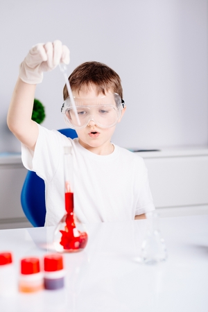 Little chemist - 7 years old boy in protective gloves and google mixing colored liquids in test tubesの写真素材