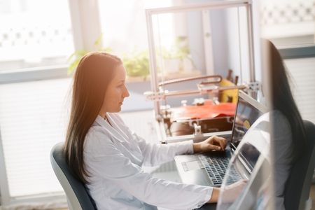 Woman in a white lab coat designs item to three dimensional printing. 3d printingの写真素材