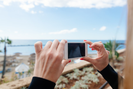 Woman photographing ocean and beach with her smartphone. Tenerife, Playa del Duque, Costa Adejeの写真素材