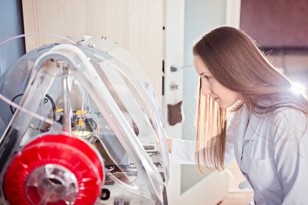 Young woman in white lab coat working with 3d printer
