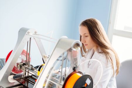 Young woman in white lab coat working with 3d printer