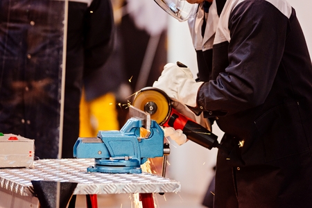Mechanic in protective gloves cutting metal with red handheld grinder