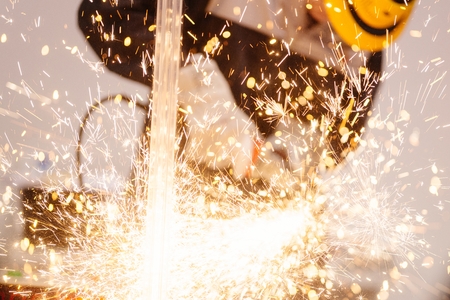 Mechanic in protective gloves cutting metal with red handheld grinder causing many sparksの写真素材