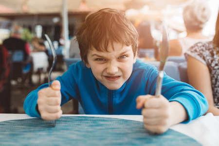 Little child boy hungry waiting for dinner in restaurant. Holding fork and knifeの写真素材