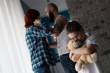 Sad child hugging his teddy bear during parents quarrel. Man about to beat his wifeの写真素材