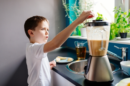 Happy child preparing fruit cocktail in kitchen. Mixing fruits in blender. Healthy eatingの写真素材