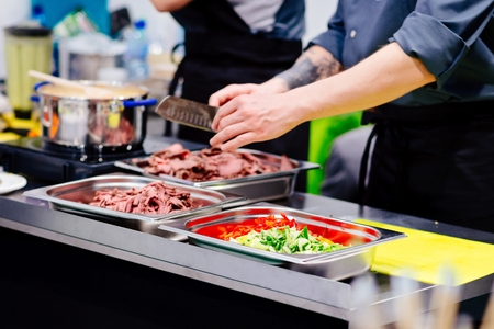 Chef cook cutting ostrich meat, paprika and cucumber in restaurant kitchenの写真素材