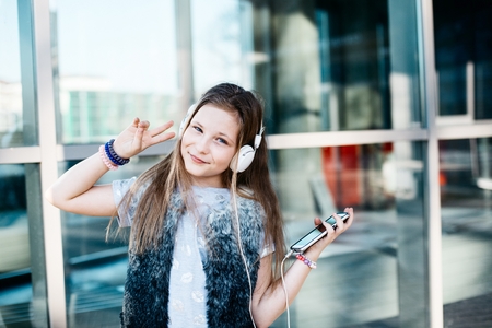 10 years old happy girl child listen to the music from her smartphone. Sunny day at cityの写真素材