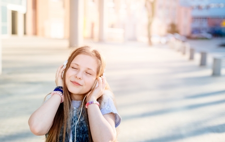10 years old happy girl child listen to the music. Sunny day at cityの写真素材
