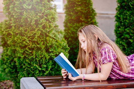 Ten years old blue eye blonde girl reading book at the bench.の写真素材