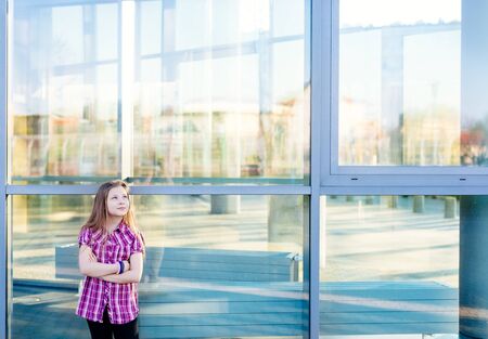 Happy ten years old blue eyed girl standing near school and looking upの写真素材