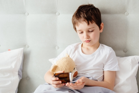Sick child boy takes medication in bed. Kid's clinic.の写真素材