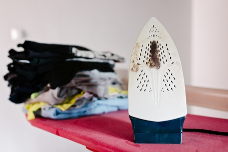 Burnt dirty modern iron on ironing board.の写真素材