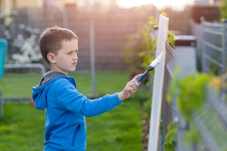 Little boy child painting the fence in garden with white paintの写真素材