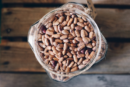 Raw pinto beans in glass jar on wooden background. Healthy diet food