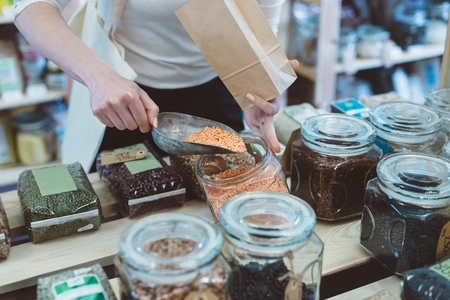 Woman puts lentil seeds into a paper bag in a healthy food storeの写真素材
