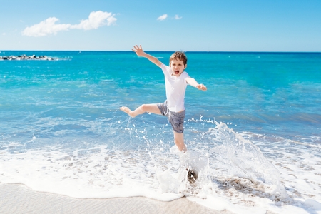 Happy child jumping and playing on the beach. Playa Del Duque, Tenerife, Canary Islands, Spainの写真素材