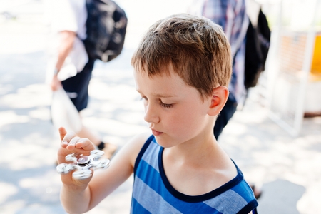 Little child boy playing with fidget spinner outdoors