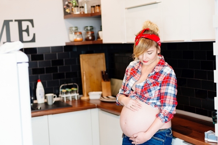 Beautiful pin up stylized young pregnant woman in kitchenの写真素材